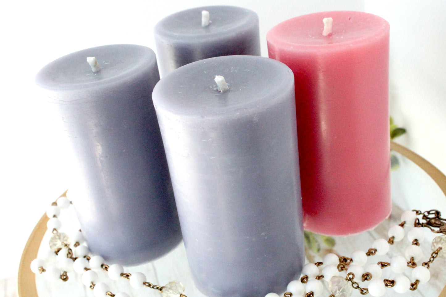 Four candles in purple and pink on a decorative surface with beads and flowers.