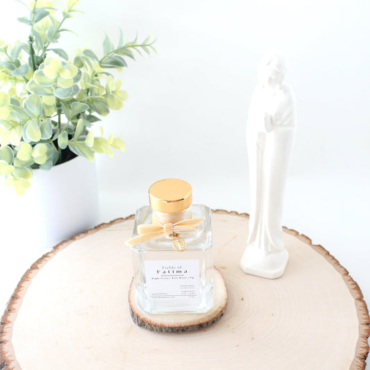 reed diffuser on wood plank with mary statue and plant in background