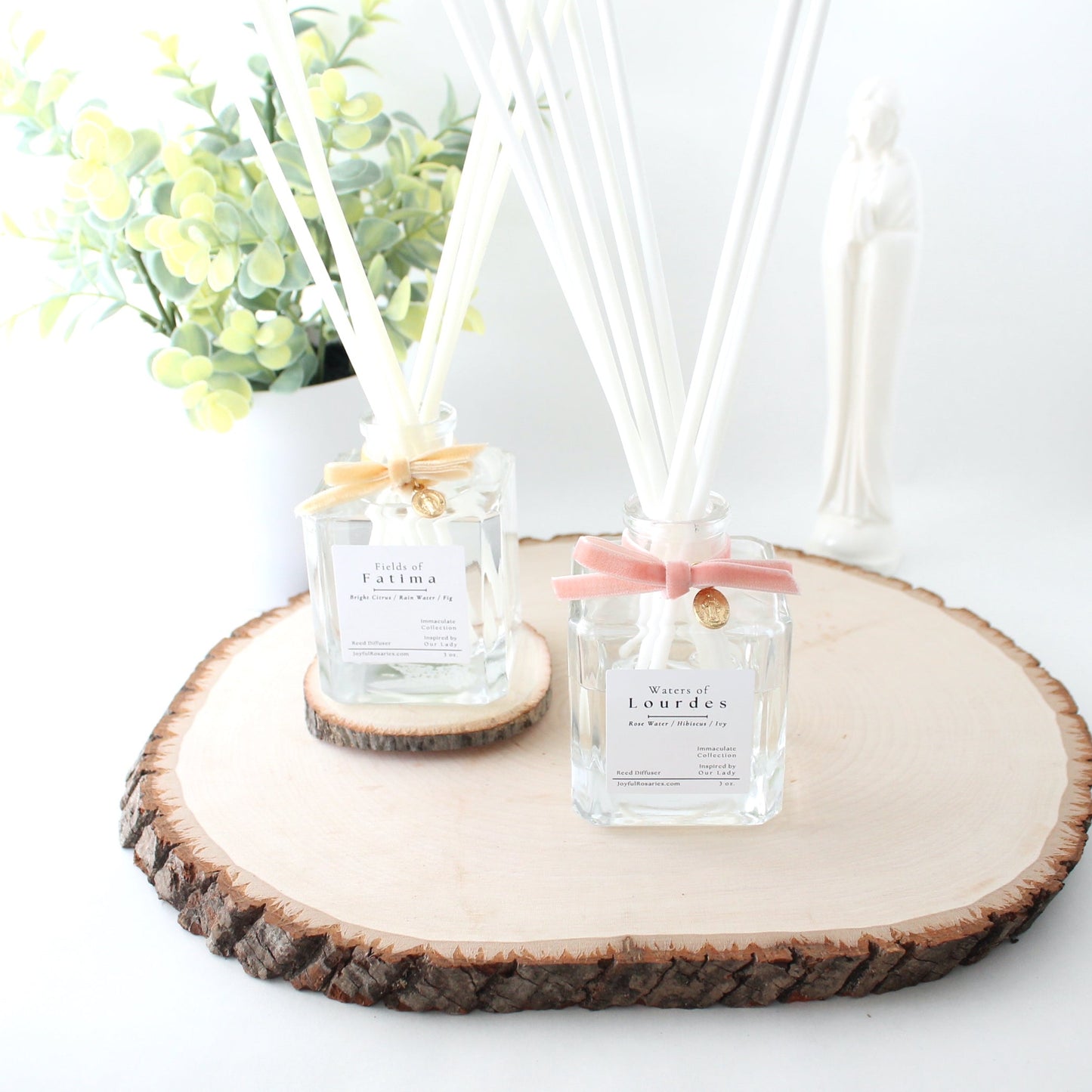 Two small glass bottles with diffusers on a wooden coaster with a white background