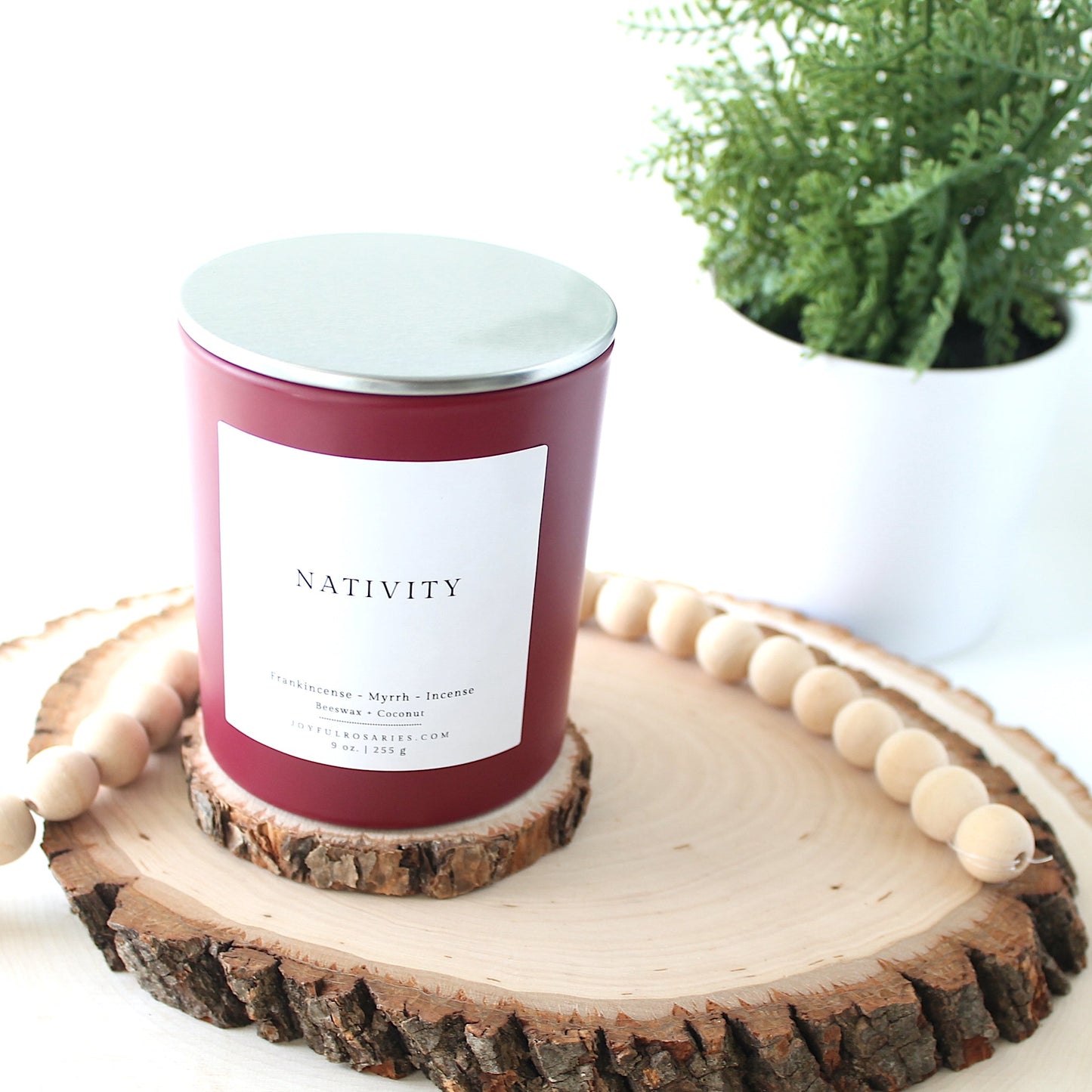 red Candle labeled 'Nativity' on a wooden coaster with a plant in the background
