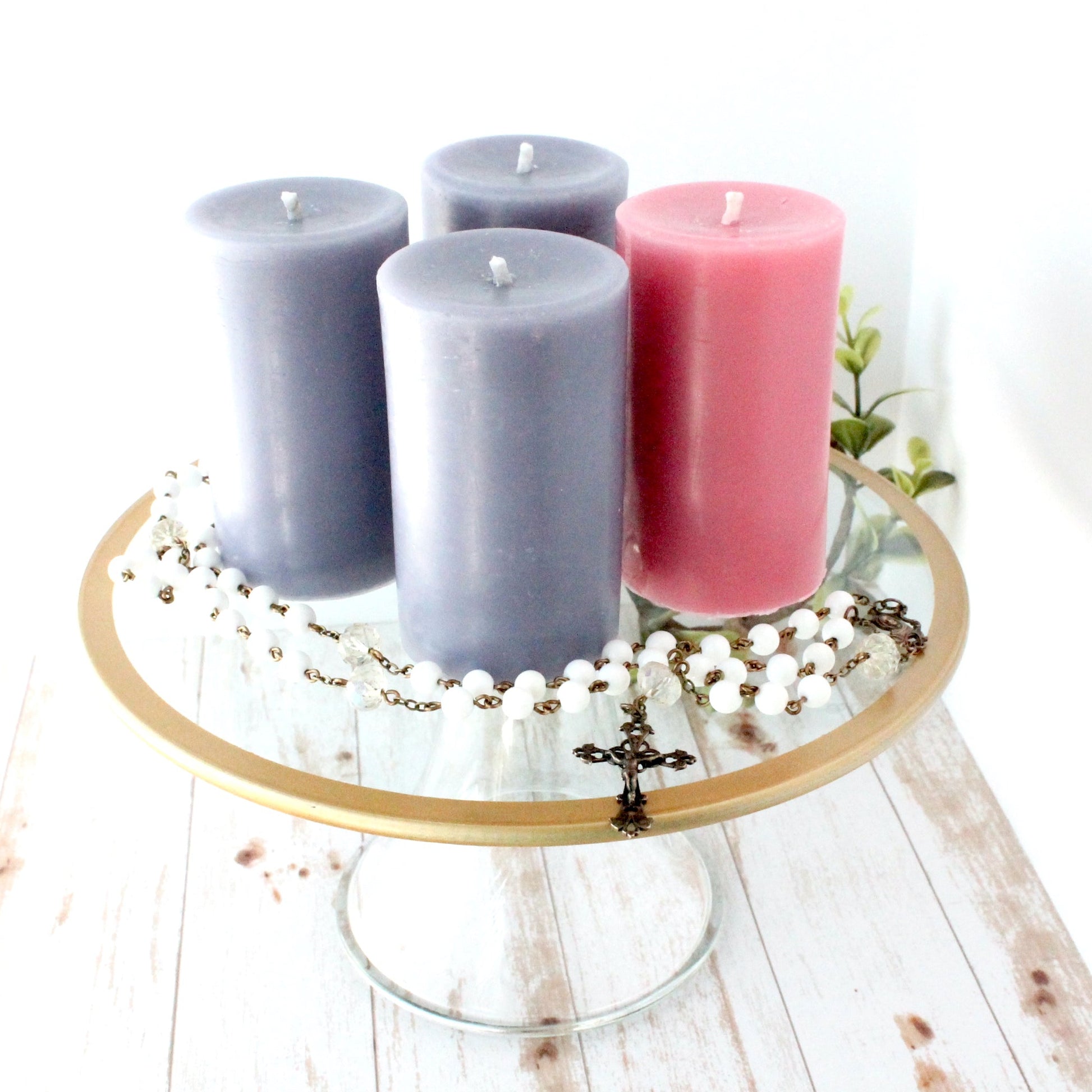 Four advent beeswax candles in purple and pink on a decorative stand with a white background