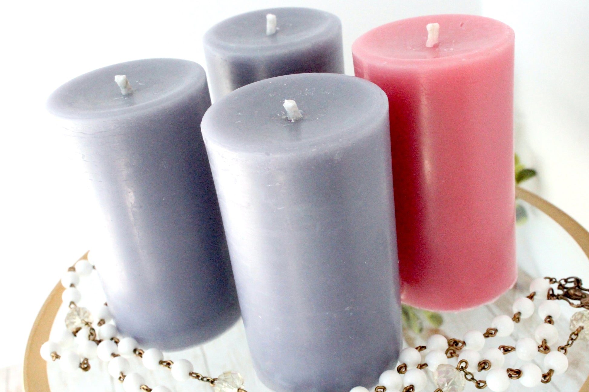 Four candles in purple and pink on a decorative surface with beads and flowers.