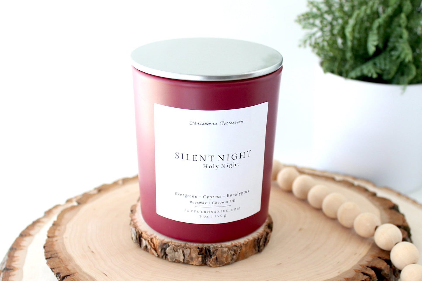 Candle labeled 'Silent Night' on a wooden coaster with a plant in the background