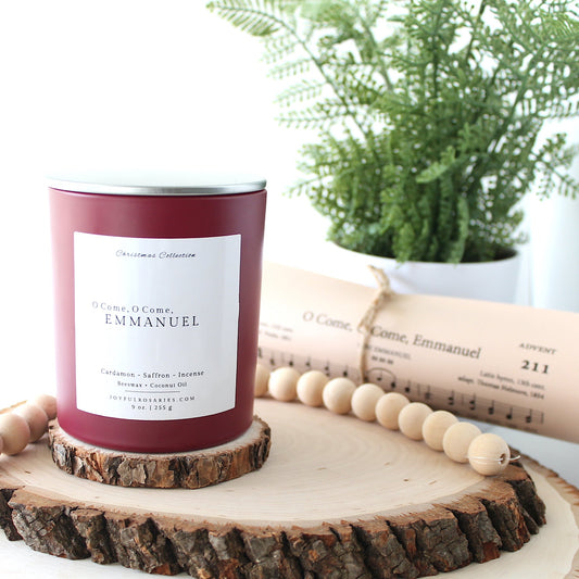 Red Candle jar with white square label on a wooden coaster next to a plant and rolled up lyrics