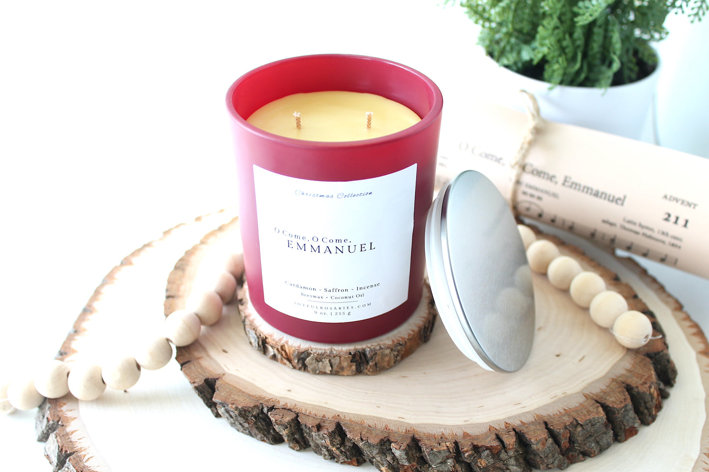 Candle with a red container and white label on a wooden coaster, surrounded by decorative elements.