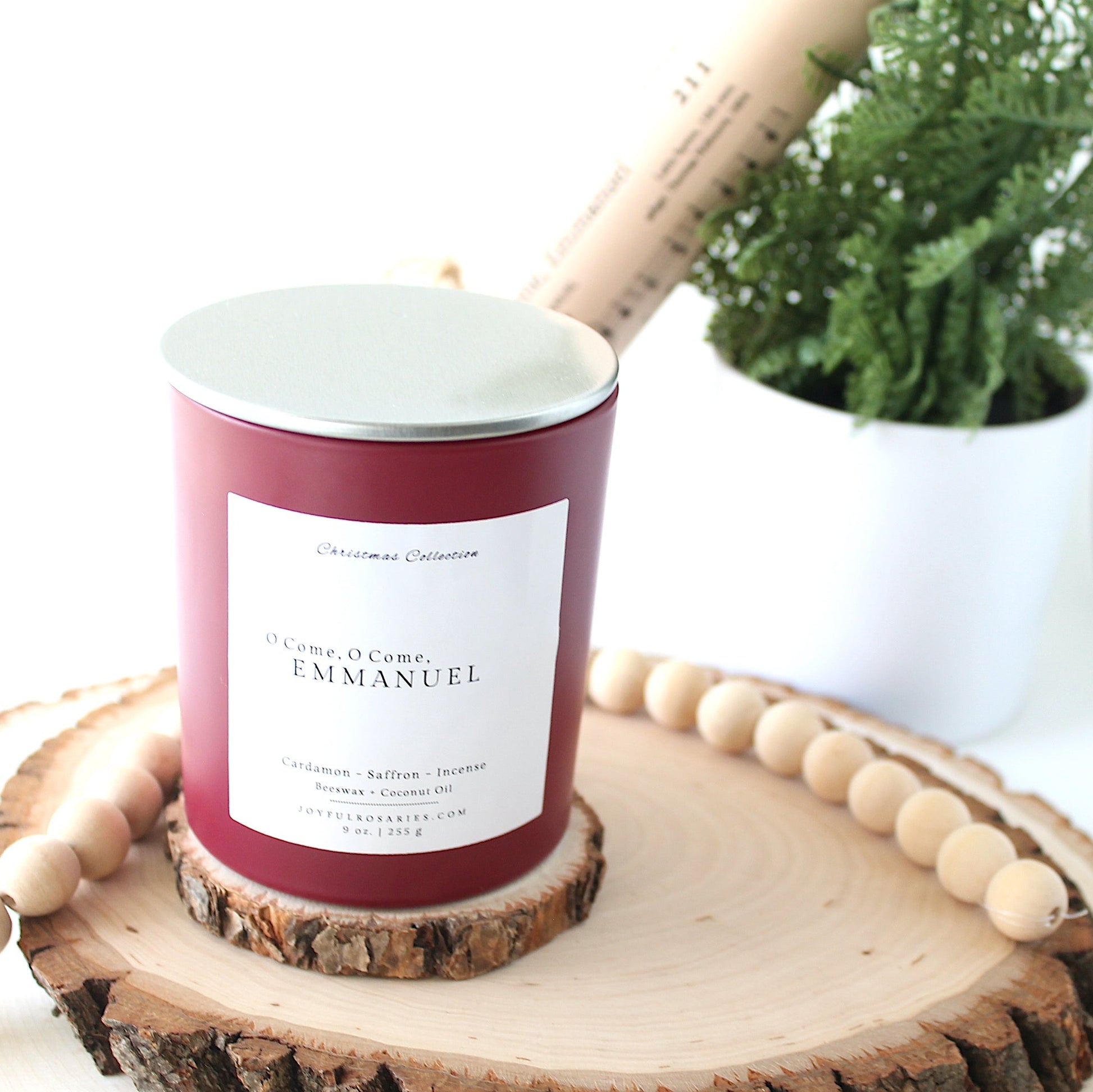 red Candle with silver lid with a label on a wooden surface next to a plant