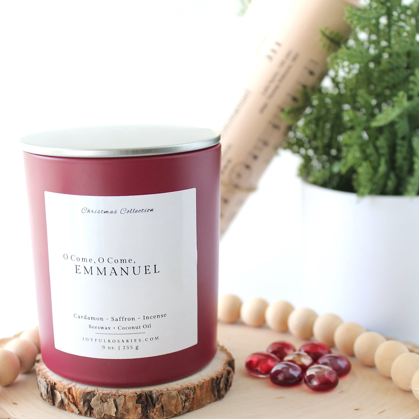 red Candle jar with silver lid with a label on a wooden surface next to a plant and red beads
