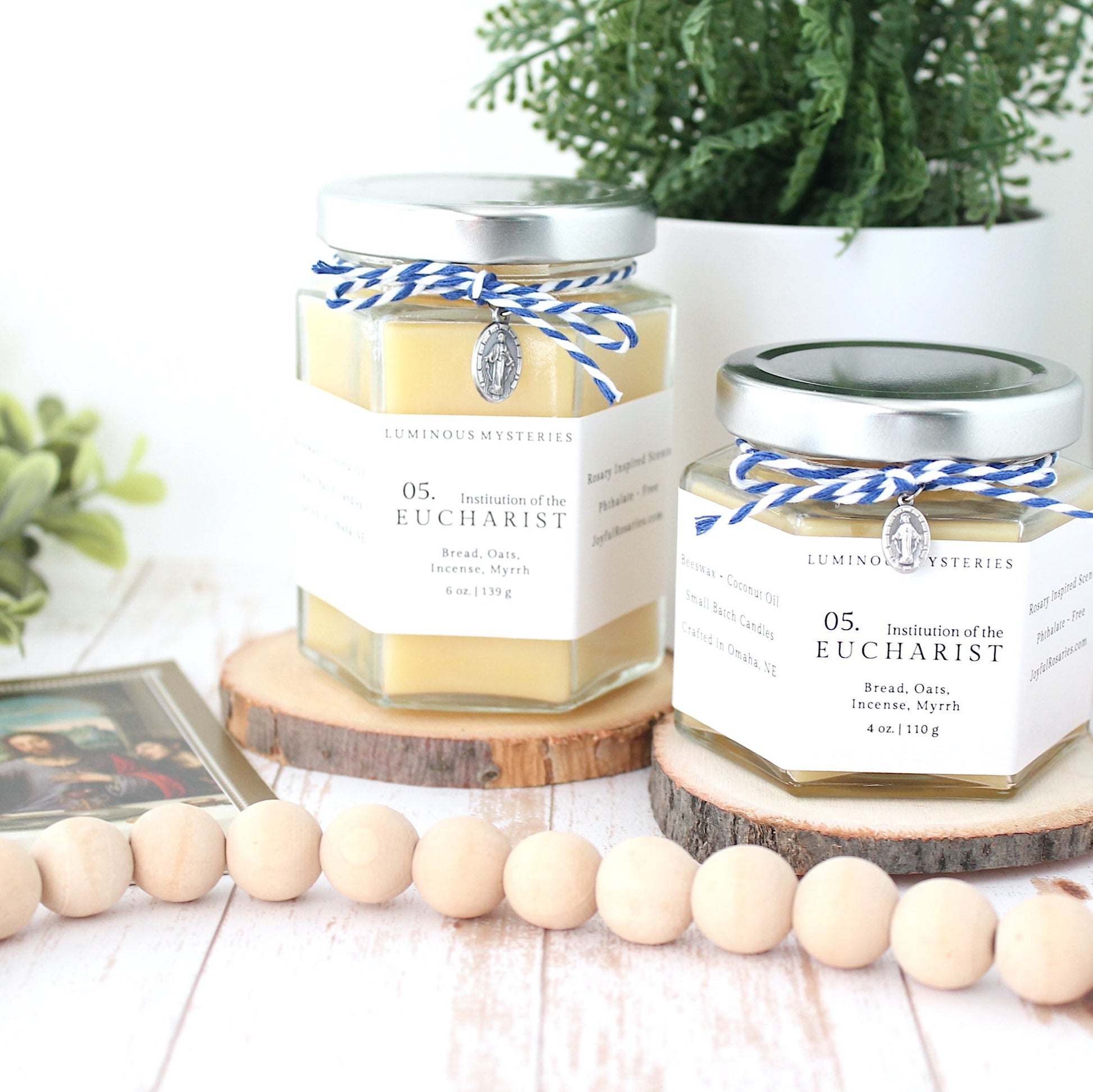Two hexagonal candles with labels on a wooden surface with plants and beads in the background.