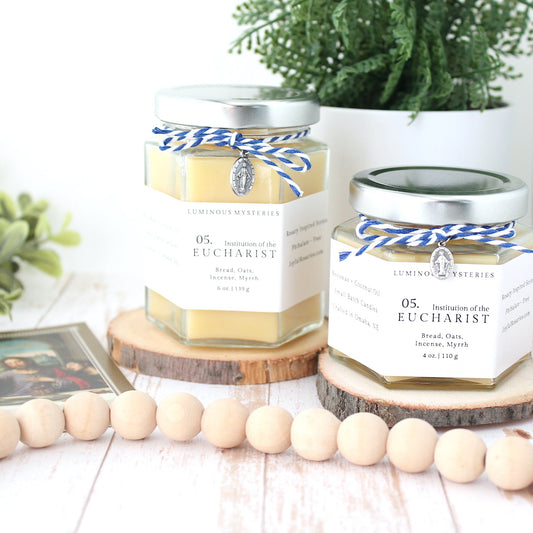 Two hexagonal candles with labels on a wooden surface with plants and beads in the background.