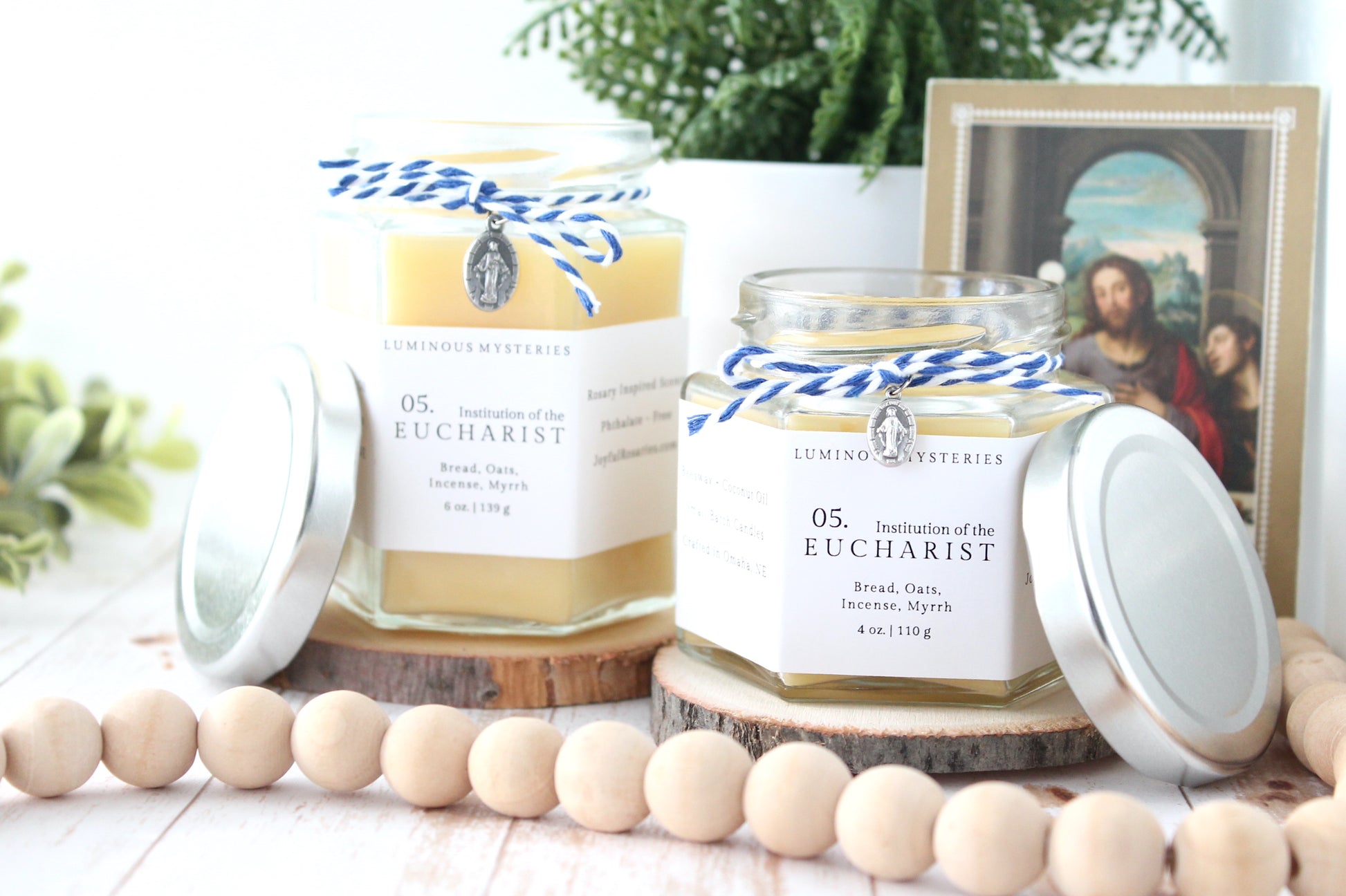 Two candles labeled 'Eucharist' from Joyful Rosaries on a wooden surface with decorative items.