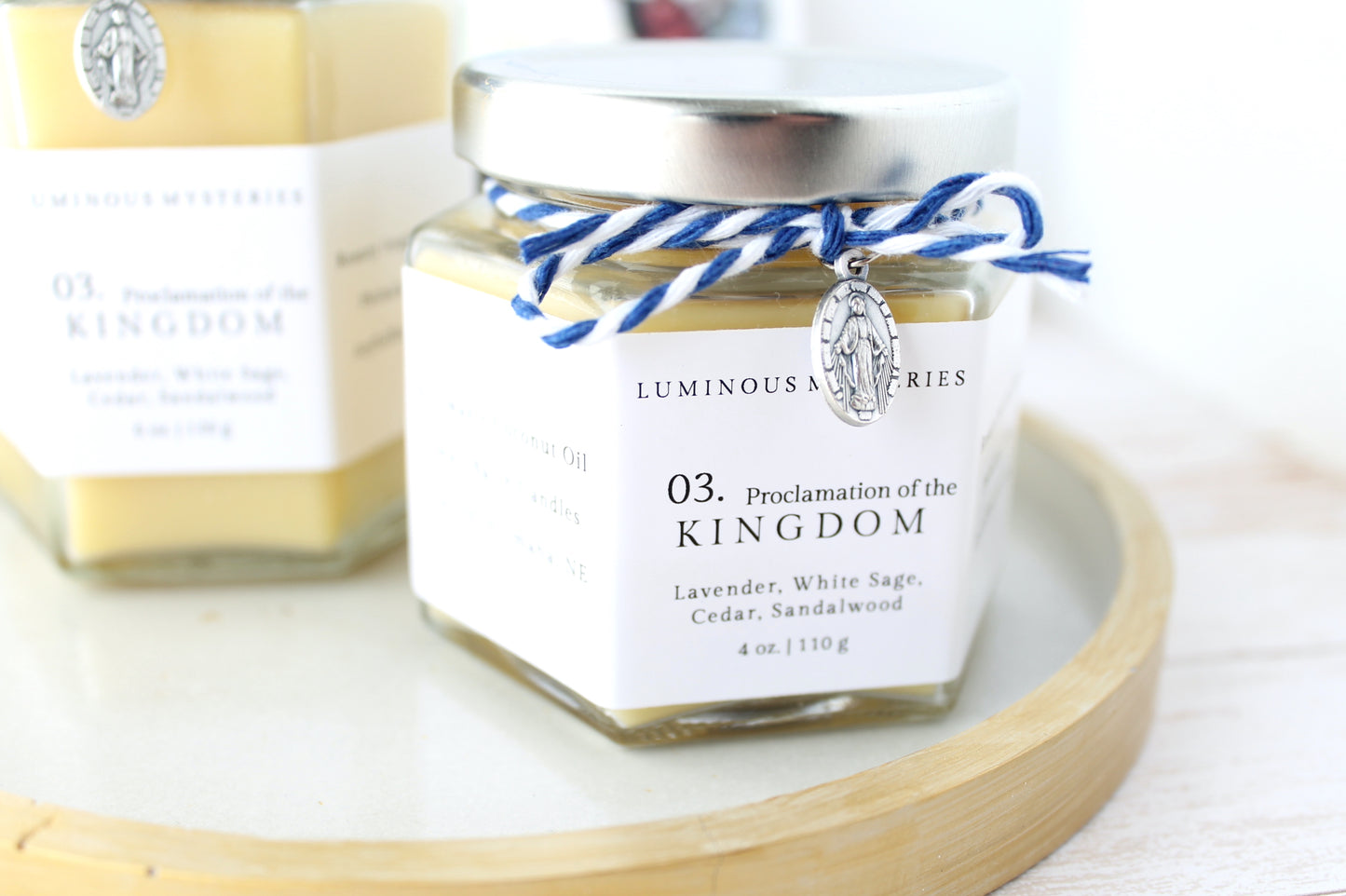 Jar of 'Proclamation of the Kingdom' candle on a white surface with a blurred background
