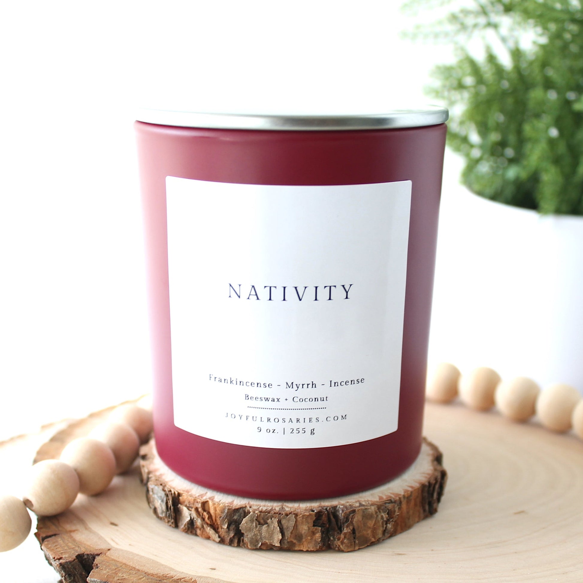 Candle labeled 'Nativity' on a wooden surface with a plant in the background