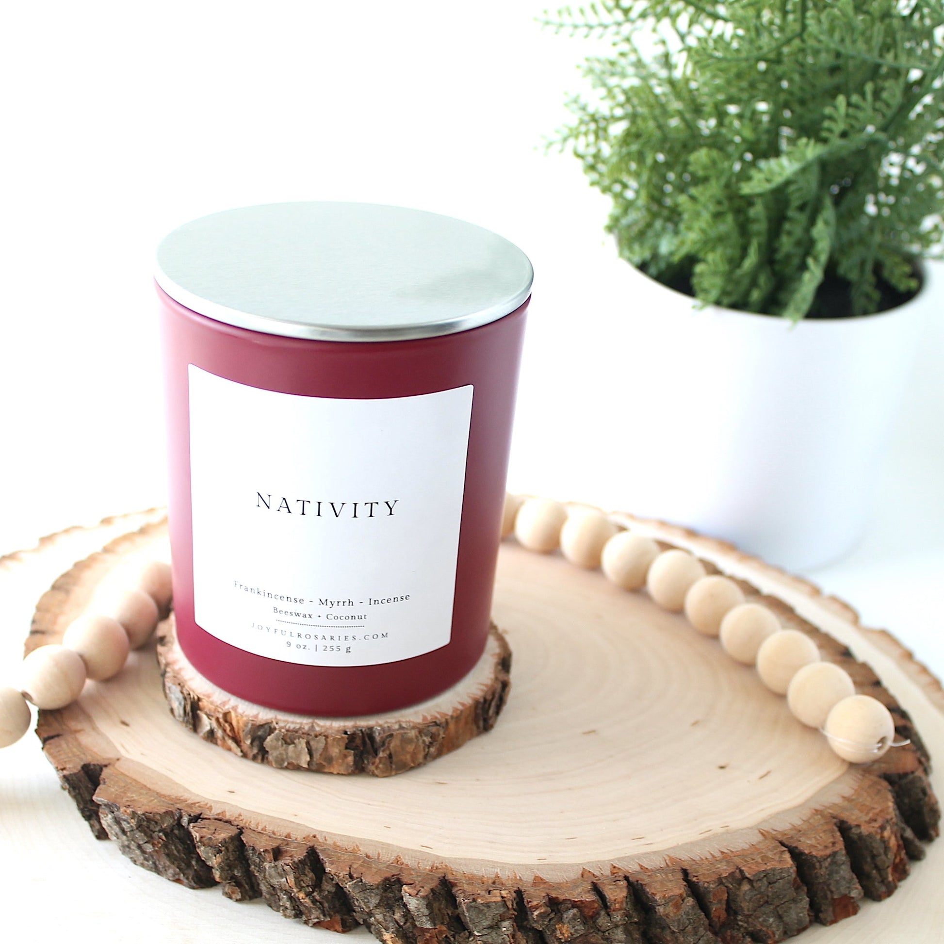 red Candle labeled 'Nativity' on a wooden coaster with a plant in the background