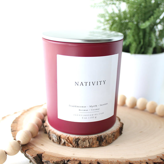 red Candle labeled 'Nativity' on a wooden coaster with a plant in the background