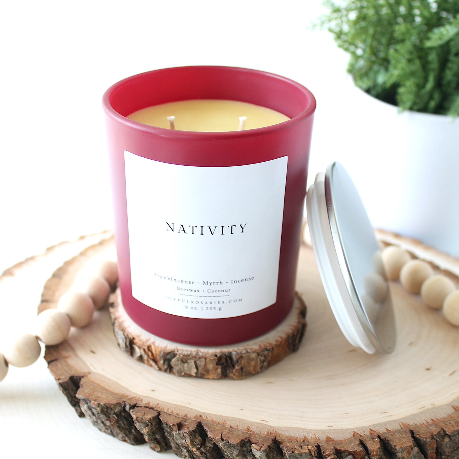 red Candle with 'Nativity' label on a wooden coaster with a plant in the background