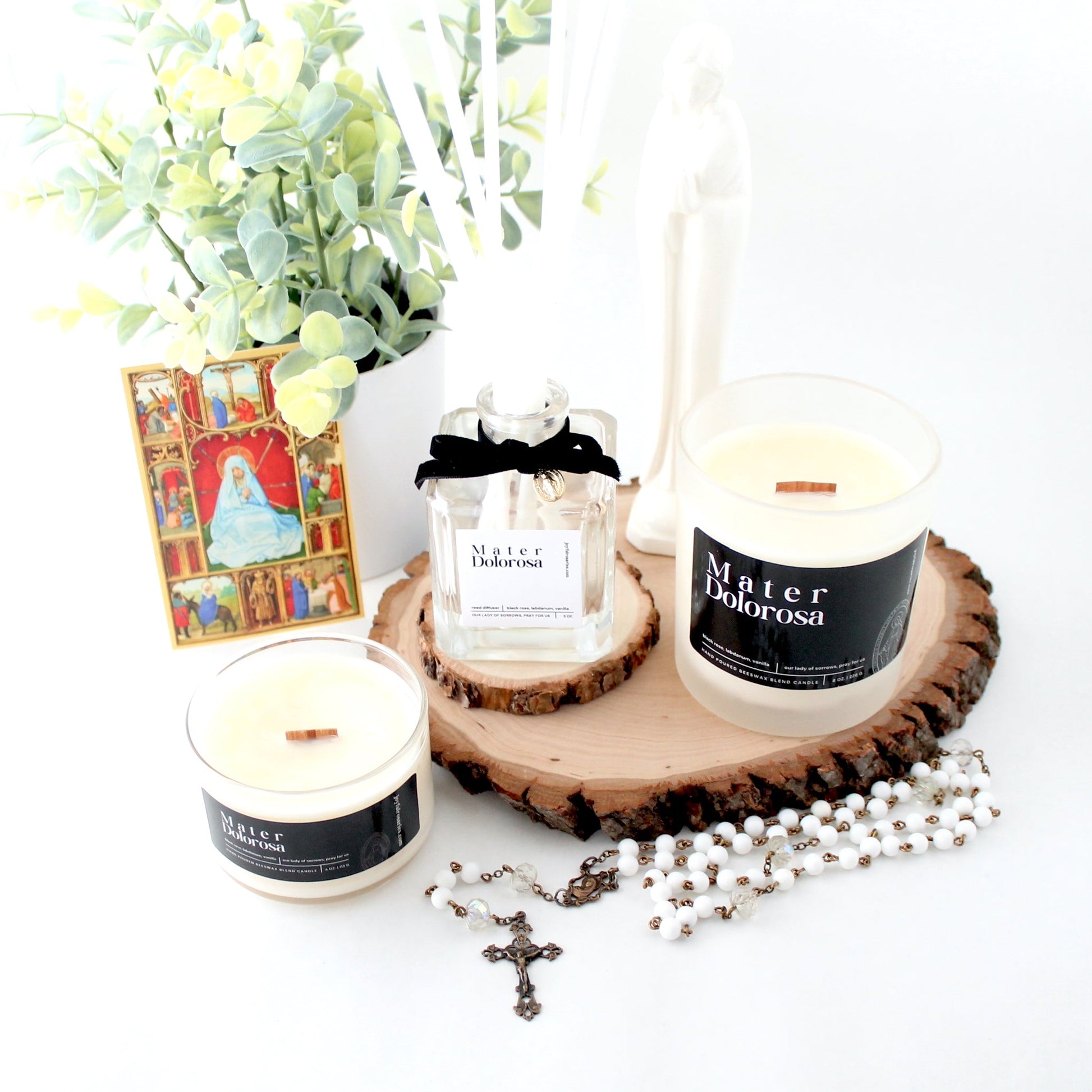 Candles with labels on a wooden coaster, surrounded by decorative items on a white surface.