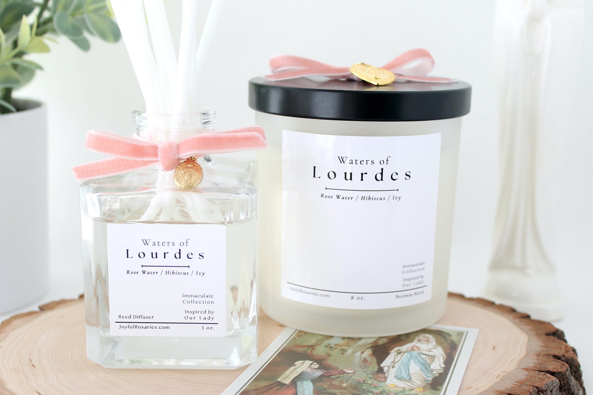 Reed Diffuser and candle labeled 'Waters of Lourdes' on a wooden surface with a plant in the background.